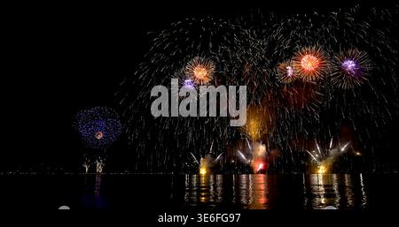 I colorati fuochi d'artificio illuminano il cielo notturno sull'acqua durante una festa nei pressi di una città in estate Foto Stock