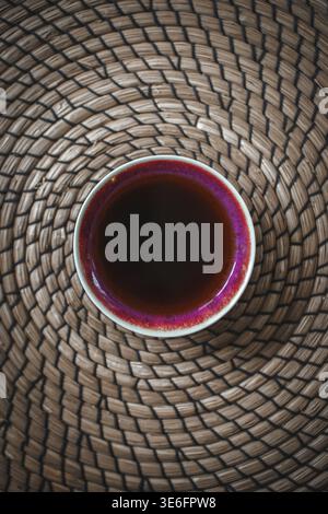 Una vista dall'alto incredibilmente rilassante di una deliziosa tazza di caffè che riposa tranquillamente su un tappeto intrecciato Foto Stock