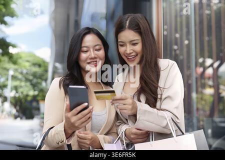 Due donne si divertono a fare shopping nel Black Friday, controllando i loro acquisti e pagamenti con smartphone e carta di credito in mano Foto Stock