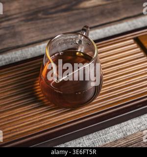Teiera di vetro finemente lavorata, elegantemente riempita con tè fumante e posizionata su un vassoio rustico in legno Foto Stock