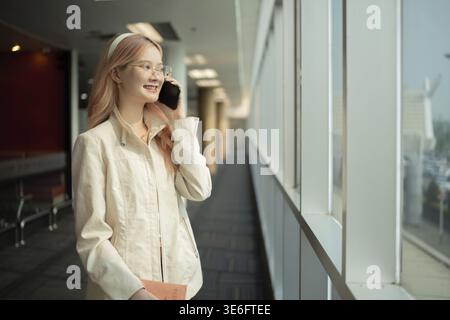 Donna asiatica che parla su smartphone nel terminale dell'aeroporto. Concetto di viaggio, comunicazione e anticipazione Foto Stock