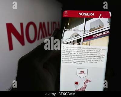 Stoccarda, Germania - 08-12-2024: Persona che detiene il cellulare con il sito web della società giapponese di servizi finanziari Nomura Holdings Inc. Con il logo. Concentrati su Foto Stock