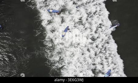 Vista aerea di Surfer nuoto a bordo vicino enorme onda blu oceano. Vista drone di un sacco di surfisti in attesa di onde. Una vista aerea dei surfisti in attesa Foto Stock