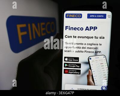 Stoccarda, Germania - 08-12-2024: Persona che detiene cellulare con pagina web della società italiana di servizi finanziari FinecoBank S.p.A. davanti al logo. Concentrati Foto Stock