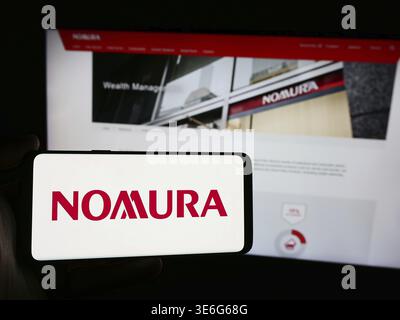 Stoccarda, Germania - 12-08-2024: Persona che detiene uno smartphone con logo della società giapponese di servizi finanziari Nomura Holdings Inc. Davanti al sito web. Foto Stock