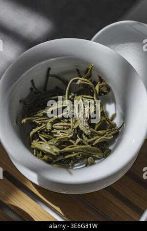 Immagine ravvicinata che raffigura foglie di tè verde fresco elegantemente esposte in una bella ciotola sotto una luce soffusa e delicata Foto Stock