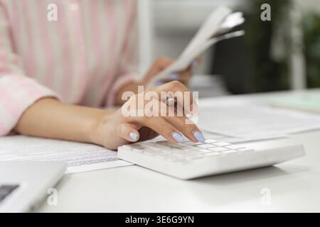 In un ufficio domestico ben illuminato, una persona lavora diligentemente sui calcoli utilizzando una calcolatrice durante la gestione dei documenti. Lo spazio di lavoro è organizzato e promo Foto Stock