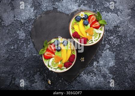 Frullato verde nelle ciotole per una sana colazione. Frullato biologico fresco a base di spinaci, banane, spirulina, tiglio e tiglio con frutti di bosco e frutta Foto Stock