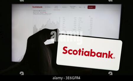 Stoccarda, Germania - 12-08-2024: Persona che detiene un telefono cellulare con logo della società finanziaria Bank of Nova Scotia (Scotiabank) davanti al business web Foto Stock