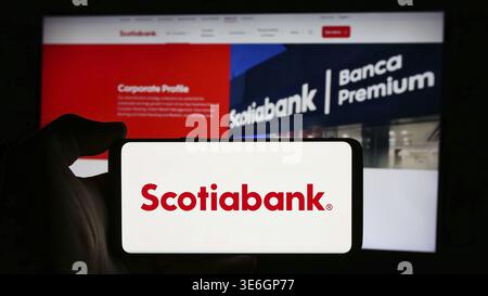 Stoccarda, Germania - 08-12-2024: Persona che detiene il cellulare con il logo della società finanziaria Bank of Nova Scotia (Scotiabank) di fronte alla pagina web aziendale Foto Stock