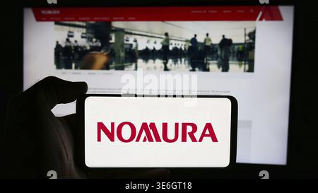 Stoccarda, Germania - 08-12-2024: Persona che detiene il cellulare con il logo della società giapponese di servizi finanziari Nomura Holdings Inc. Davanti alla pagina web. F Foto Stock
