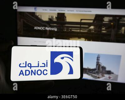 Stoccarda, Germania - 12-08-2024: Persona in possesso di smartphone con logo della società petrolifera Abu Dhabi National Oil Company (ADNOC) davanti al sito Web. Concentrati Foto Stock