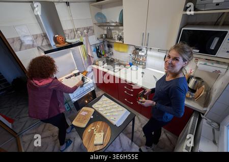 Due amiche di mezza età cucinano croissant di pasta sfoglia insieme come uno mette il vassoio nel forno Foto Stock