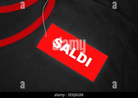 Cartellino rosso su una t-shirt grigia e rossa con la parola italiana “saldi” scritta in bianco. Foto Stock