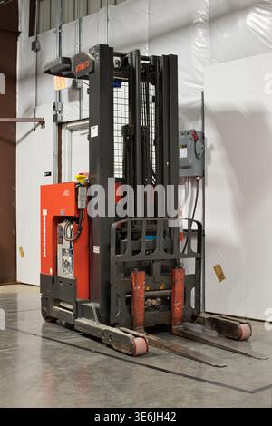 Houston, Texas USA 04-05-2026: Carrello elevatore a forche retrattile sulla stazione di ricarica della batteria parcheggiata all'interno del magazzino. Foto Stock