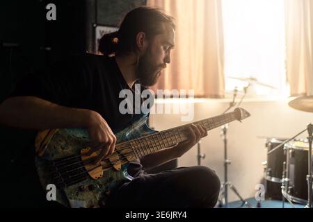 Bassista che suona il basso in studio, sessione di registrazione, musicista concentrato, pratica di performance dal vivo, stile di vita artistico, retroilluminazione calda. Foto Stock
