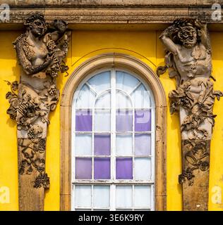 Facciata barocca ornata con finestra ad arco su parete gialla, fiancheggiata da figure scolpite e rilievi floreali in pietra Foto Stock