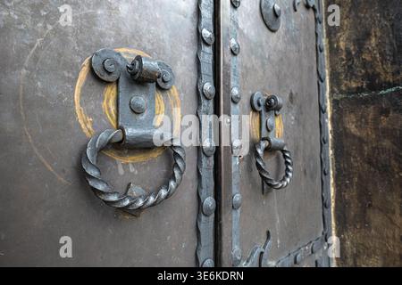 Primo piano di due battitori ad anello in metallo ritorto su una porta in metallo scuro e resistente agli agenti atmosferici con dettagli dei rivetti Foto Stock