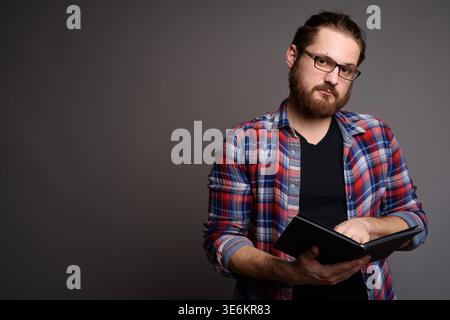 Ritratto in studio di un giovane uomo caucasico con barba e occhiali che tengono in mano un libro e guardano la macchina fotografica. Offre ampio spazio di copia per le attività didattiche, Foto Stock