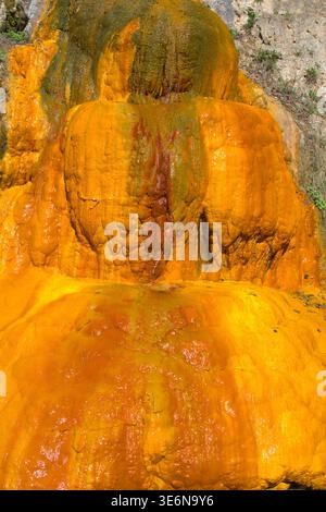 Primo piano di una terrazza minerale in travertino arancione con acqua termale fluente, depositi di ferro e zolfo Foto Stock