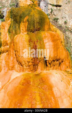 Primo piano di una terrazza minerale in travertino arancione con acqua termale fluente, depositi di ferro e zolfo Foto Stock