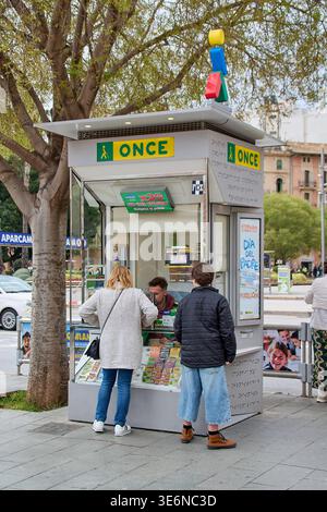 Maiorca. Spagna - 07 aprile 2026: Una moderna lotteria si erge su un marciapiede della città con persone che acquistano i biglietti. Il logo ufficiale e il braille Foto Stock