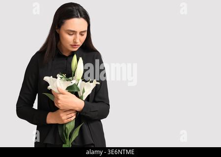 Giovane donna con bouquet funebre di fiori di giglio su sfondo bianco Foto Stock