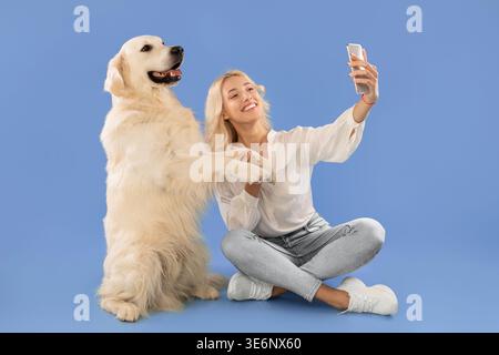 Una giovane donna porta Selfie con il suo Golden Retriever Dog su sfondo blu Foto Stock