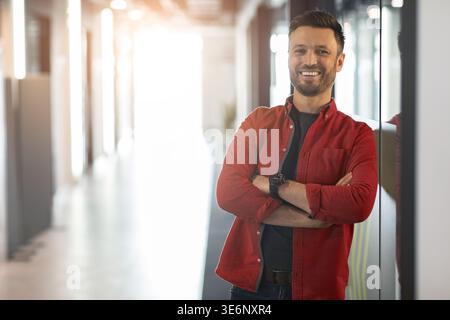 Young Man sorride mentre si trova in un corridoio dell'ufficio durante le ore diurne Foto Stock