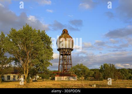 Una vecchia torre d'acqua arrugginita contro un cielo blu con nuvole e circondata da alberi, Ilseder Huette, Ilsede, Peine District, bassa Sassonia, Germania Foto Stock
