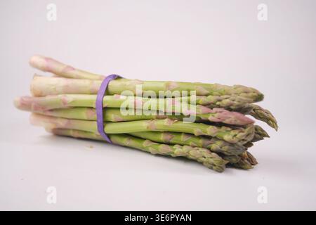 Asparagi legati con banda viola su superficie bianca Foto Stock
