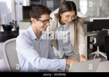 Due colleghi sorridenti collaborano al progetto congiunto nello spazio di lavoro aziendale Foto Stock