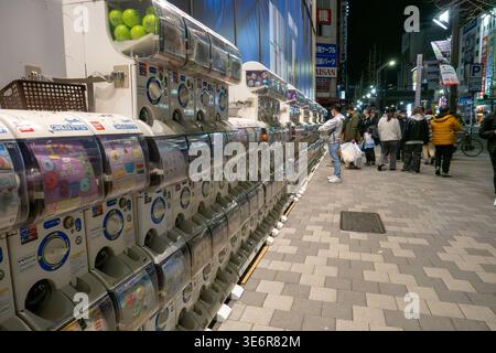 17 marzo 2026, Tokyo, Giappone: Una lunga fila di distributori automatici di capsule giocattolo, noti come gachapon, fa la fila di un marciapiede nel quartiere Akihabara di Tokyo, in Giappone, di notte. I pedoni curiosano e fanno shopping lungo la strada trafficata nel popolare quartiere dell'elettronica e degli anime. I distributori automatici di giocattoli a capsula, noti come gachapon, distribuiscono piccoli giocattoli da collezione in capsule sigillate con un elemento a sorpresa randomizzato. Presenti in tutto il Giappone nei portici, nei negozi e nelle stazioni ferroviarie, sono popolari sia tra i bambini che tra gli adulti per la loro novità e varietà. (Immagine di credito: © Shawn Goldberg/SOPA Images via ZUMA Press Wire) EDI Foto Stock