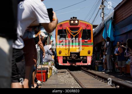SAMUT SONGKHRAM, TAILANDIA-Mar 28, 2026: Treno diesel che passa dal mercato degli ombrelli pieghevoli alla piattaforma, atmosfera del mercato ferroviario, vista frontale Foto Stock