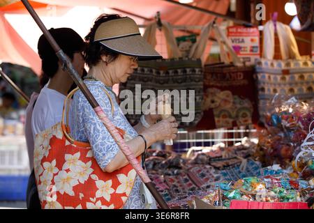 SAMUT SONGKHRAM, THAILAND-Mar 28, 2026: Turista femminile che esplora il mercato di strada in Thailandia, atmosfera commerciale del mercato locale, profilo laterale, a Maeklong Foto Stock