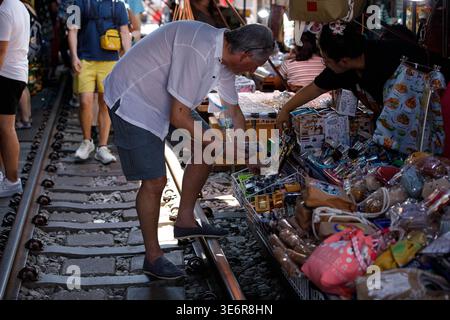 SAMUT SONGKHRAM, TAILANDIA-Mar 28, 2026: Turista maschile che sceglie i prodotti presso il mercato ferroviario di Rom Hub, profilo laterale, mercato di Mae Klong. Foto Stock
