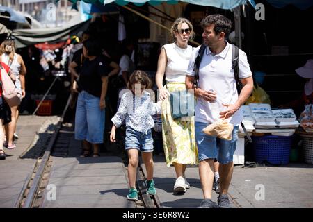 SAMUT SONGKHRAM, TAILANDIA-Mar 28, 2026: Famiglia turistica che acquista beni economici al mercato degli ombrelli pieghevoli, vista frontale, a Maeklong. Foto Stock