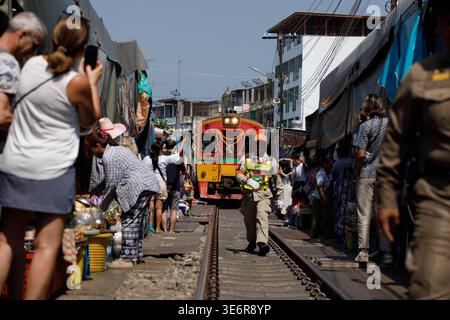 SAMUT SONGKHRAM, TAILANDIA-Mar 28, 2026: Turisti in piedi che scattano foto del treno che si muove attraverso il mercato verso la piattaforma, vista frontale Foto Stock