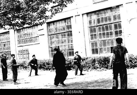 Sloviansk, 1950 anni. Il territorio dell'impianto di armatura e isolamento (AIZ). I lavoratori delle fabbriche sovietiche si impegnano con entusiasmo in una partita amichevole di pallavolo all'aperto vicino agli edifici industriali, in attesa dell'inizio di una festosa manifestazione pubblica. I giocatori guardano in alto in previsione della palla volante durante questo momento ricreativo attivo. Questa autentica fotografia d'archivio in bianco e nero mette in risalto gli sport di squadra, l'attività fisica quotidiana e la vibrante eredità storica del pacifico Donbas. Foto Stock