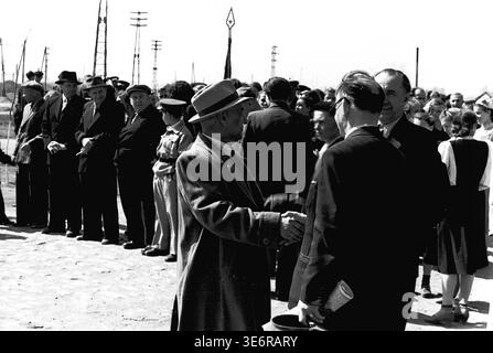 Sloviansk, 1950 anni. Il territorio vicino all'impianto di armatura e isolamento (AIZ). Due distinti uomini sovietici stringono la mano in primo piano durante un affollato raduno pubblico all'aperto. Sono circondati da colleghi di fabbrica e cittadini locali che si preparano per una grande manifestazione di massa festosa, con bandiere alte e bandiere visibili contro il cielo luminoso. Questa autentica fotografia d'archivio in bianco e nero cattura perfettamente i saluti formali, la solidarietà della comunità e la vibrante eredità storica del pacifico Donbas. Foto Stock