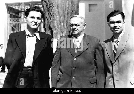 Sloviansk, 1950 anni. All'esterno dell'impianto di armatura e isolamento (AIZ). Tre fiduciosi uomini sovietici vestiti con abiti formali affilati posano insieme accanto a un tronco di albero grezzo nel cortile della fabbrica. I colleghi attendono con calma l'inizio di una manifestazione di massa festosa in una giornata molto luminosa e soleggiata. Questa fotografia d'archivio in bianco e nero altamente autentica mostra splendidamente la moda maschile della metà del secolo, le forti amicizie professionali, l'amministrazione della fabbrica e il ricco patrimonio culturale del pacifico Donbas. Foto Stock