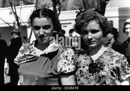 Sloviansk, 1950 anni. Il territorio dell'impianto di armatura e isolamento (AIZ). Due belle giovani operaie sovietiche posano per un affascinante ritratto ravvicinato alla luce del sole prima di partecipare a una manifestazione di massa festosa. Le donne indossano eleganti abiti floreali con le classiche acconciature intrecciate a metà del XX secolo. Questa fotografia d'archivio espressiva in bianco e nero mostra perfettamente l'ottimismo giovanile, l'autentica moda femminile, la vera amicizia e l'eredità duratura del pacifico Donbas. Foto Stock