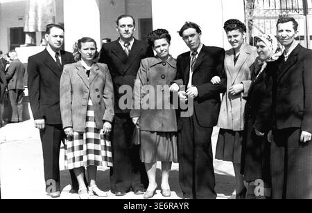 Sloviansk, 1950 anni. Il territorio vicino all'impianto di armatura e isolamento (AIZ). Un gruppo esteso di otto operai sovietici, che abbracciano generazioni diverse, si riunisce per un ritratto collettivo memorabile prima di partecipare a una manifestazione pubblica festosa. Gli uomini e le donne sono vestiti con una varietà di abiti autentici della metà del secolo, tra cui abiti, gonne a quadri e velo. Questa fotografia d'archivio in bianco e nero altamente espressiva conserva meravigliosamente l'unità della comunità e la storia del pacifico Donbas. Foto Stock
