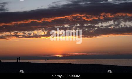 Tramonto dorato su una spiaggia di ciottoli con sagome di persone e mare Foto Stock