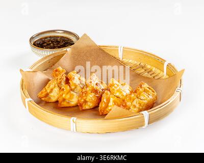 Appetitoso cibo asiatico. Gnocchi fritti dorati croccanti serviti in una vaporiera di bambù con salsa di soia scura. Composizione minimalista con luminoso, cle Foto Stock