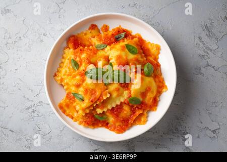 Ravioli italiani con salsa di pomodoro e foglie di basilico fresco serviti su un piatto bianco Foto Stock