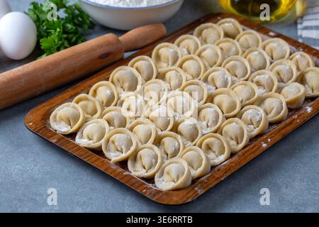 Polpette di Pelmeni crude fatte a mano su un vassoio di legno con spilla e farina sullo sfondo Foto Stock