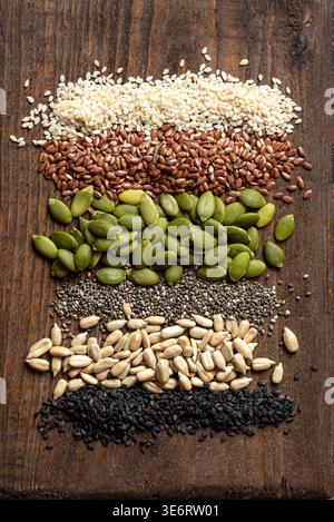 Assortimento di semi su sfondo in legno, vista dall'alto. Ingredienti alimentari sani. Semi di zucca, sesamo bianco e nero, chia, semi di girasole e lino Foto Stock