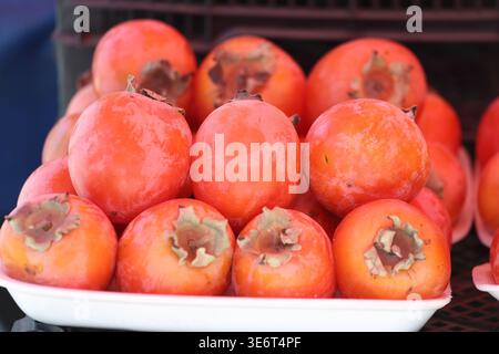 Cachi cinese (Diospyros kaki) in un contenitore in un mercato aperto. Primo piano sulla frutta di cachi cinese matura Foto Stock