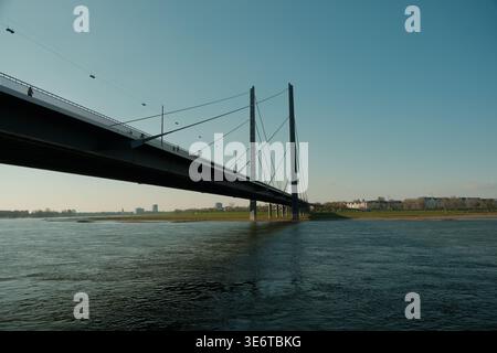 Una spettacolare vista a basso angolo di un moderno ponte strallato che si estende attraverso un ampio fiume verso una sponda erbosa sotto un vasto e limpido cielo blu. Foto Stock